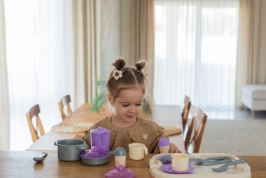 Young girl enjoying playtime with toy dishes on a sunny day indoors.