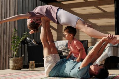 Father and kids doing yoga outdoors on a patio, balancing poses together.